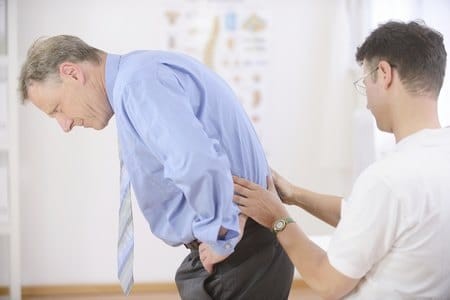 Доктор осматривает нижнюю часть спины пациенту Доктор осматривает нижнюю часть спины пациенту