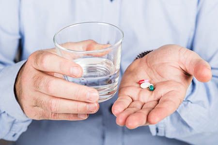 таблетки и стакан воды в руках у мужчины